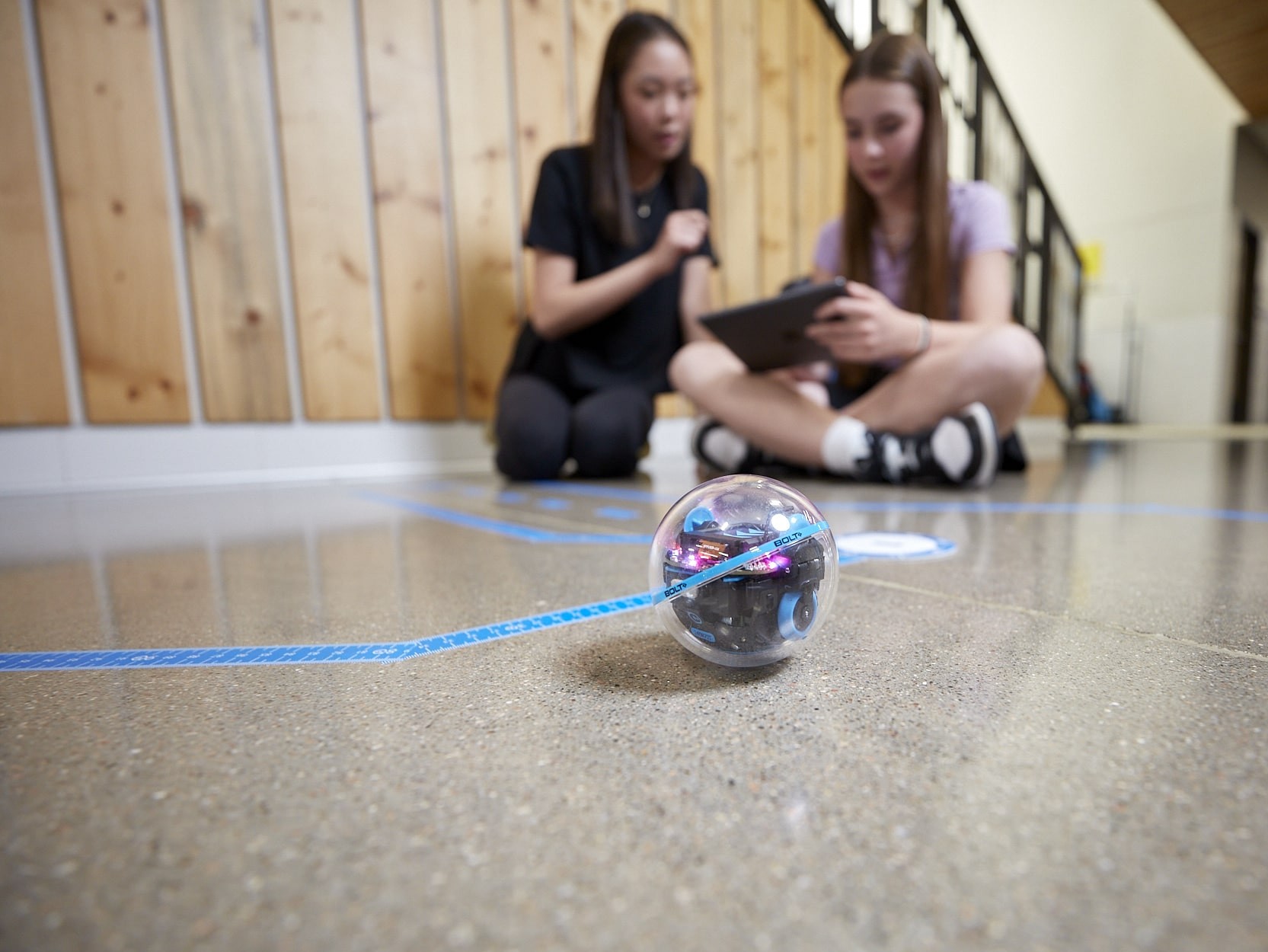 Zwei Mädchen, die auf dem Boden sitzen und mit dem Roboter BOLT+ von Sphero spielen