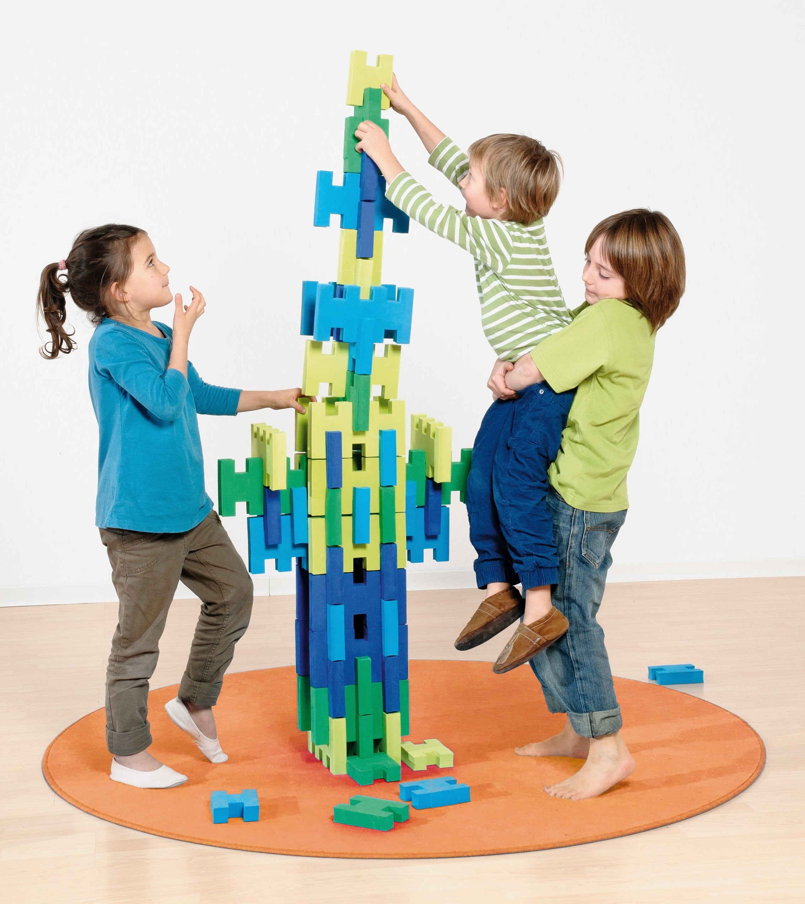 Drei Kinder bauen aus grünen und blauen Bausteinen einen Turm