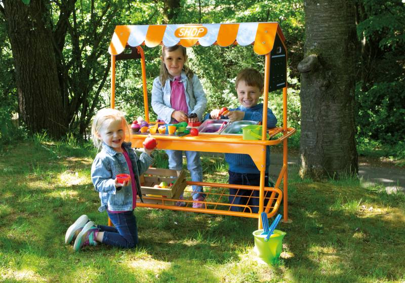 Hier sieht man drei Kinder, die im Freien mit einem Eisdielen Stand spielen