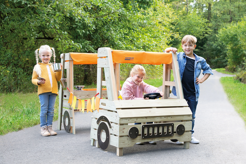 Hier sieht man dre kleine Kinder, die mit einem Kinderauto im Freien spielen