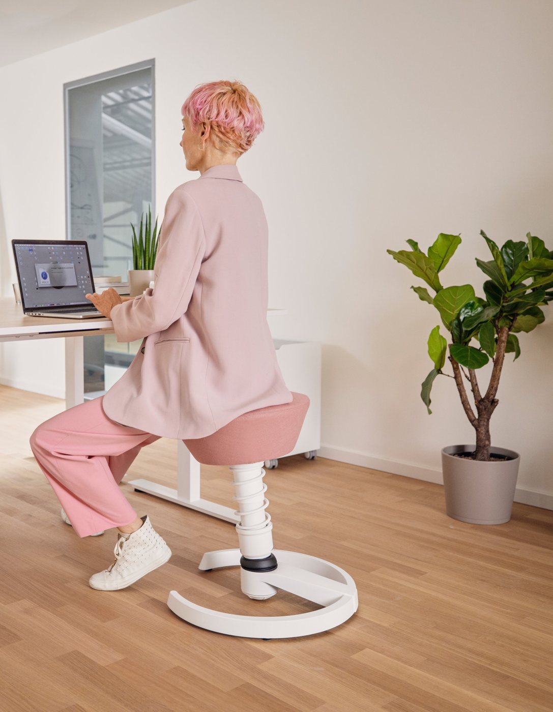 Frau sitzt auf einem rosafarbenen Aeris Swopper am Laptop