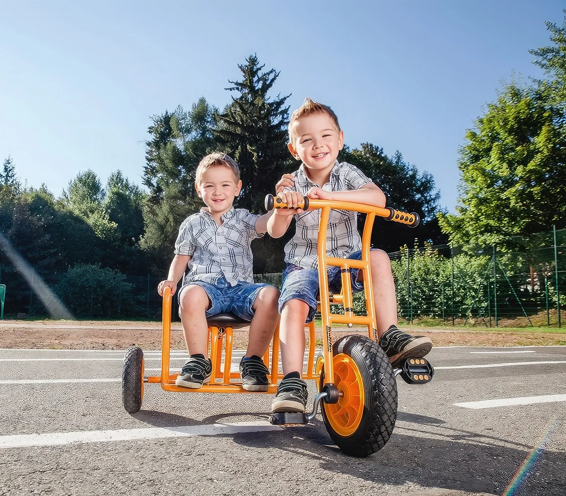 Hier sind zwei kleine Jungs die draußen zusammen auf einem Dreirad fahren, das Dreirad hat zwei Sitze