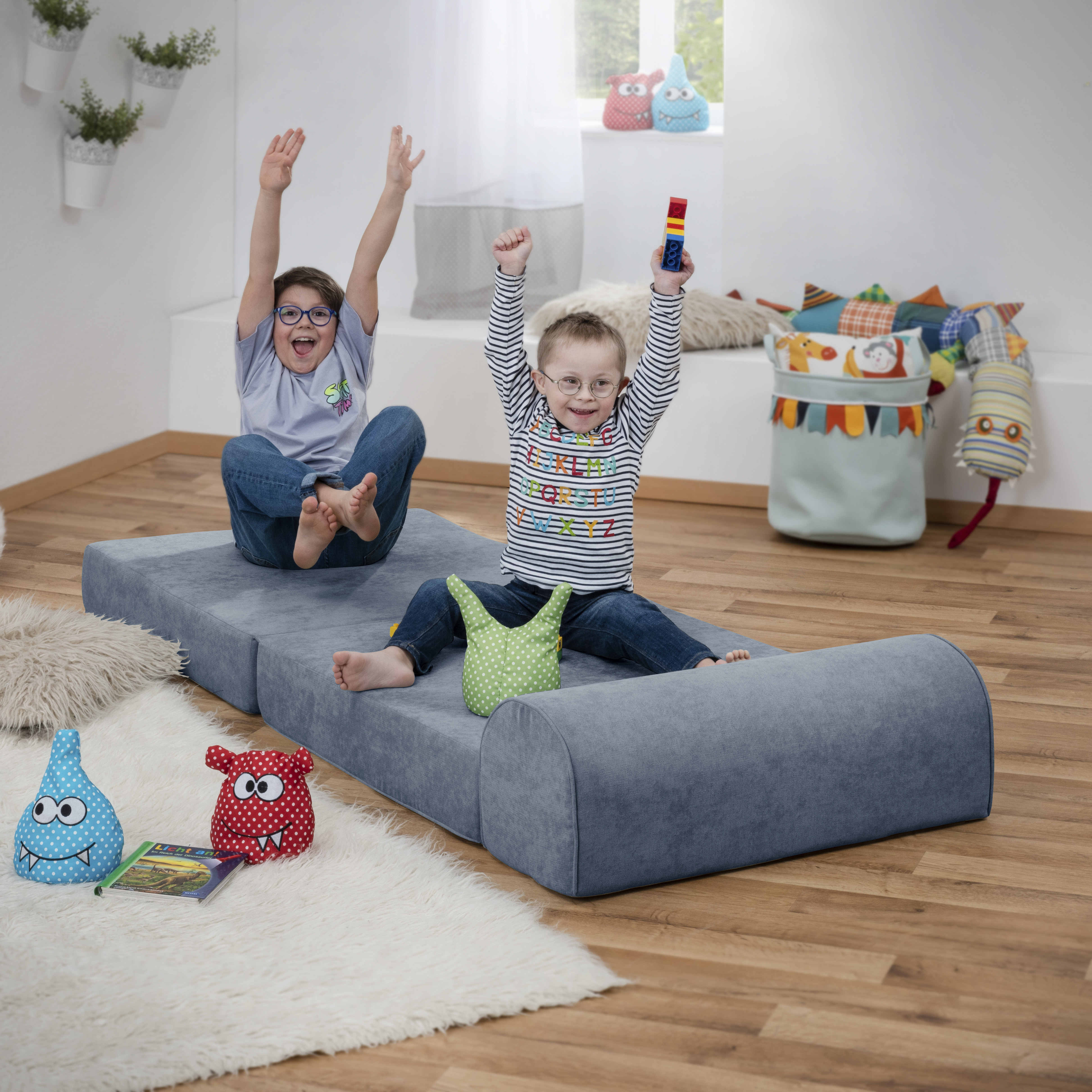 Auf dem Bild sind zwei KInder, die auf einem Sofa sitzen und die Arme in die Luft reißen 
